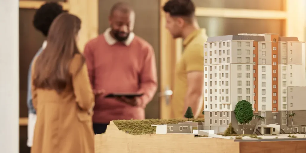 Lançamentos imobiliários: Lançamentos imobiliários: A composição da imagem apresenta um grupo de pessoas em um ambiente interior, em segundo plano, com foco principal em um maquete de um edifício.