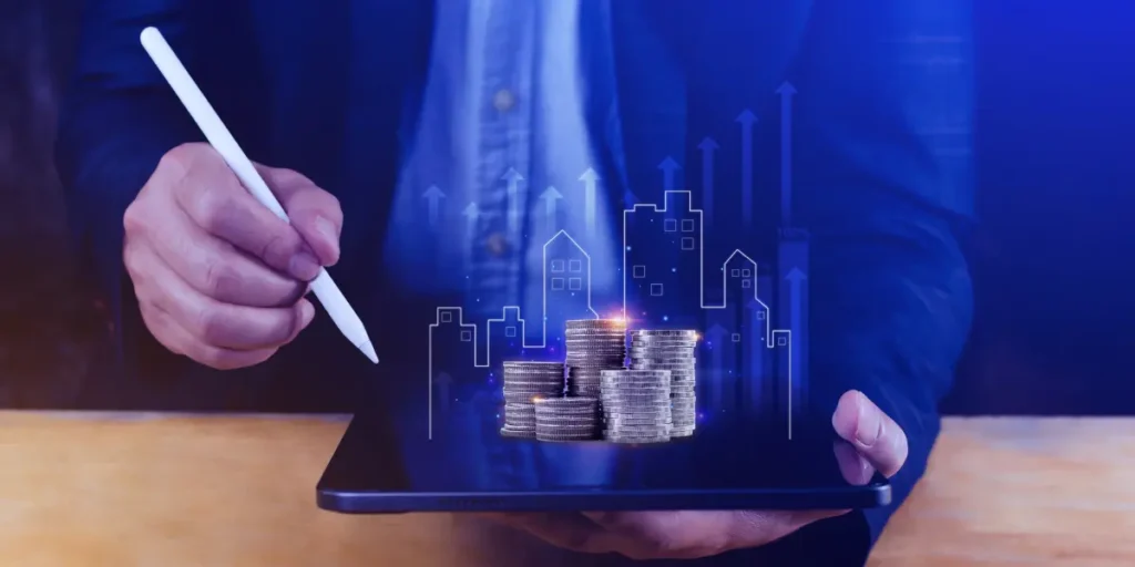 Precificação de imóveis Precificação de imóveis: A imagem do tronco de um homem segurando uma caneta digital em umas das mãos e um tablet na outra, no qual uma ilustração digital retrata pilhas de moedas, edifícios estilizados e setas ascendentes em cima do tablet.