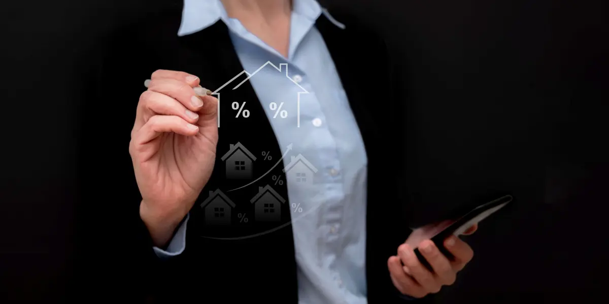 Precificação de imóveis: A composição mostra uma mulher vestindo um paletó preto e uma camisa azul clara, em um fundo preto, segurando um telefone na mão direita e uma caneta na mão esquerda. Ela está desenhando no ar, em frente a uma tela translúcida com gráficos de casas e porcentagens.