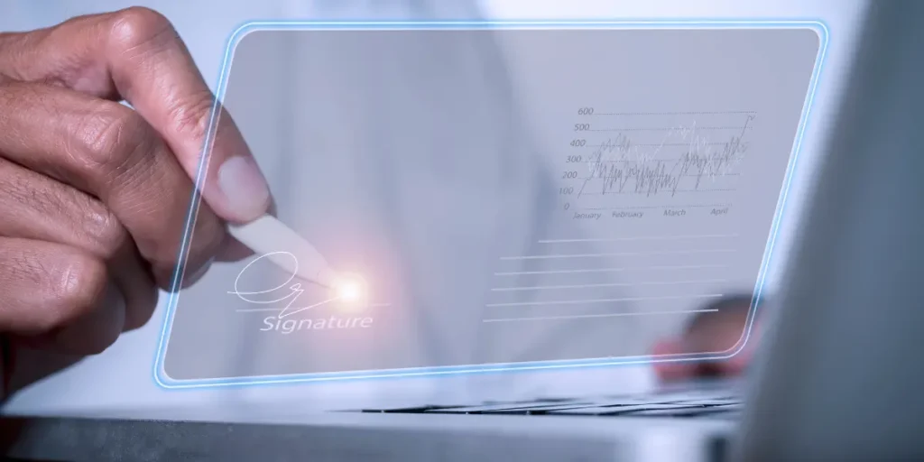 Assinatura eletrônica imobiliária Assinatura eletrônica imobiliária:
A composição foca em um close-up da mão de uma pessoa segurando uma caneta digital, assinando um documento que aparece na tela do laptop. A tela é transparente e exibe a assinatura em um layout limpo, com um gráfico de dados ao lado.