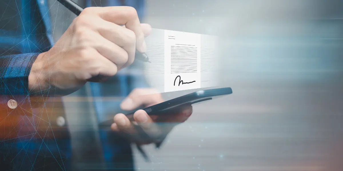 Assinatura eletrônica imobiliária: A composição foca nas mãos de uma pessoa, vestindo uma camisa, segurando um smartphone com um documento digital flutuando sobre ele. A mão direita segura uma caneta, aparentemente assinando o documento, enquanto a mão esquerda segura o smartphone.