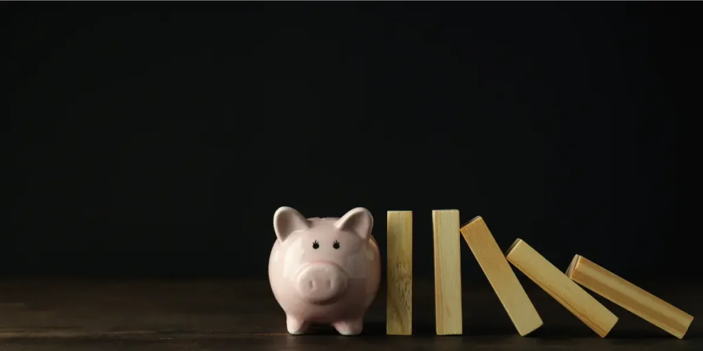 Gatilhos mentais para o mercado imobiliário Gatilhos mentais para o mercado imobiliário: imagem mostra um porquinho de cofre. Ao lado dele alguns pedaços de madeira um ao lado do outro, sendo que dois estão em pé e três caindo.