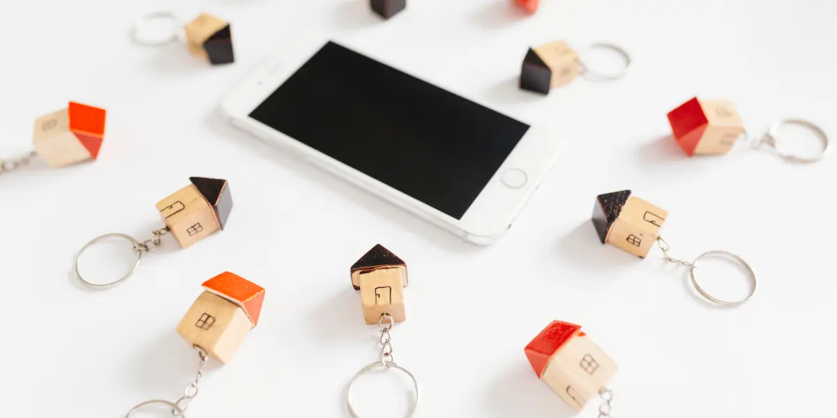 Qualificação de leads imobiliários: imagem mostra um smartphone ao centro de uma mesa, com vários chaveiros em formato de miniatura de casa ao redor do aparelho.