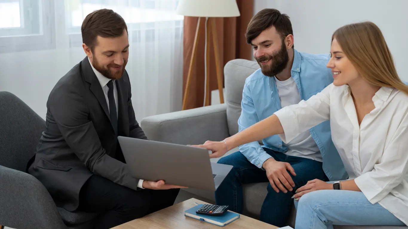 Corretor de imóveis apresenta opções em um notebook para um casal sentado no sofá, durante atendimento em ambiente interno, com clima profissional e acolhedor. gestão de parcerias imobiliárias