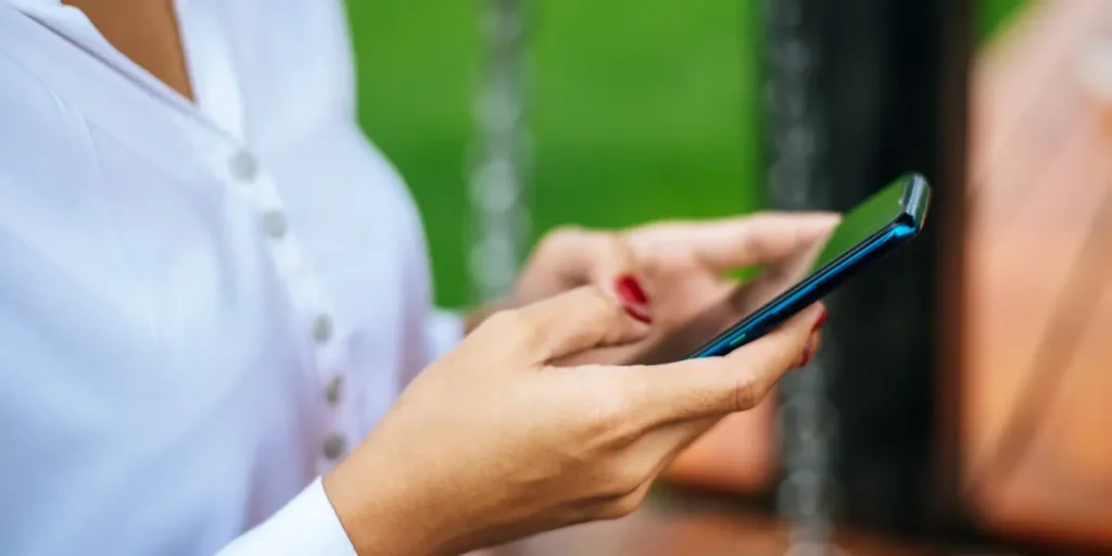 Cadência de vendas: imagem mostra o busto de uma mulher de lado, vestindo uma camisa branco, que segura um celular com as duas mãos para frente.